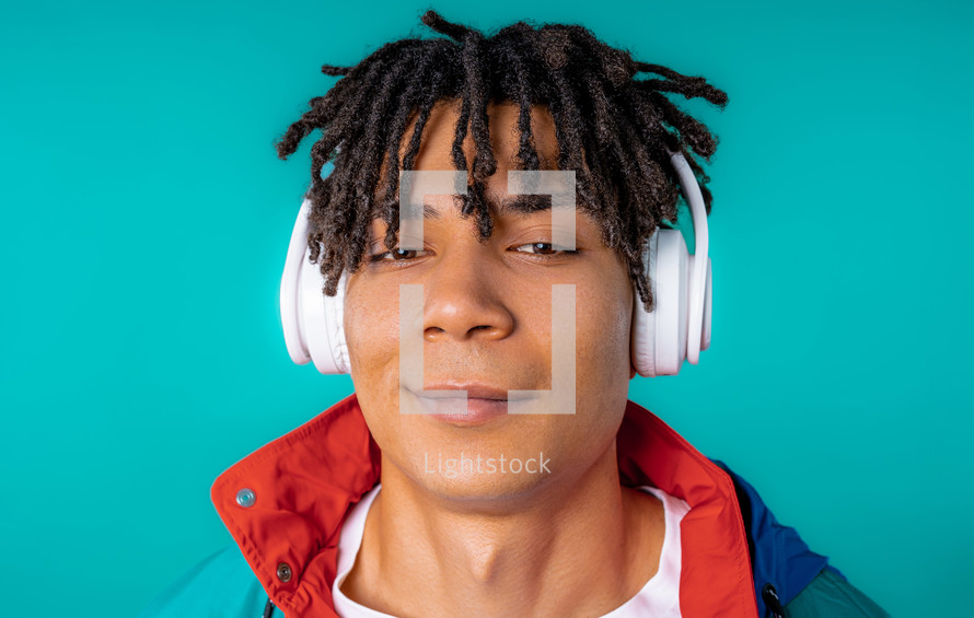 Positive young african american man listening music, enjoying dance with headphones on blue studio background. Radio, wireless modern sound technology, online player. High quality. 