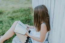 teen girl reading a Bible leaning against a fence 