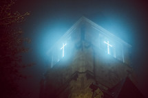 glowing cross light from a church on a foggy night 