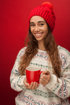 a woman in a winter sweater and hat holding a mug