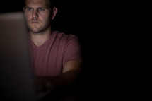 A man illuminated by the light from a computer.