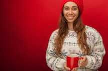 a woman in a sweater and beanie holding a mug 