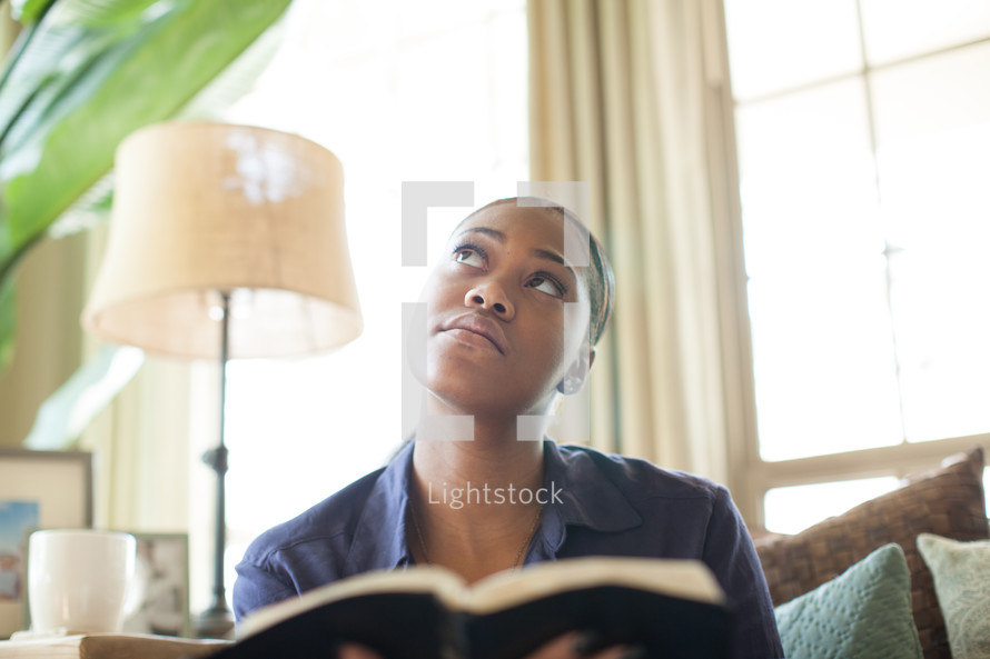African-American woman reading a Bible and looking up to God 