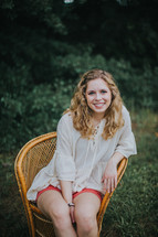portrait of a smiling teen girl sitting in a wicker chair outdoors 
