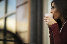 a young woman sipping a cup of coffee and looking upward.
