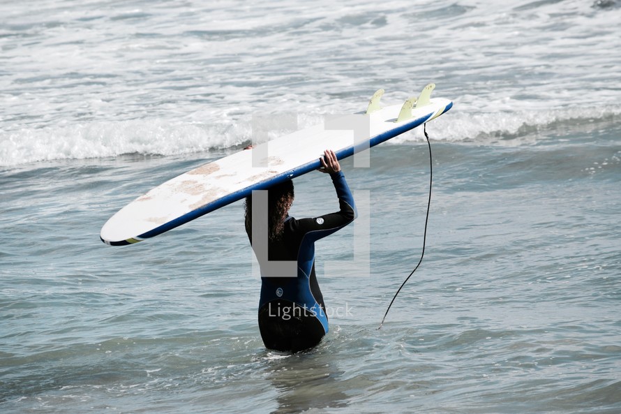 a female surfer carrying her surfboard into the ocean 