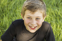 a smiling boy child sitting in tall grass 
