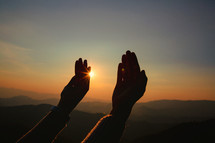 Woman raising her hands in prayer at sunset