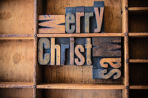 Wooden letters spelling "Merry Christmas" on a wooden bookshelf.