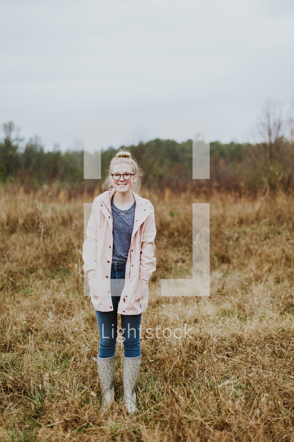 teen girl in rain boots standing in a field 