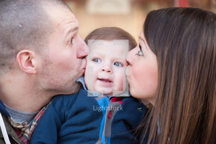 a mother and father kissing their infant son on the cheeks 