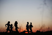 silhouettes of young adults running outdoors at sunset 