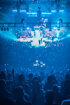 fans in a stadium and a cross shaped stage at a concert 