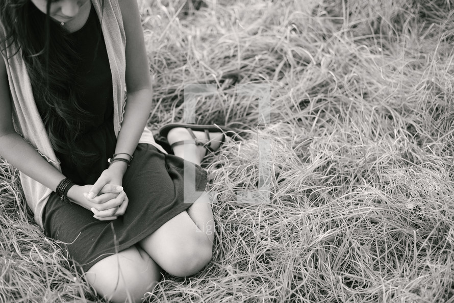 young woman kneeling praying in grass 