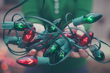 A woman holds a tangle of red and green Christmas lights in her hands.