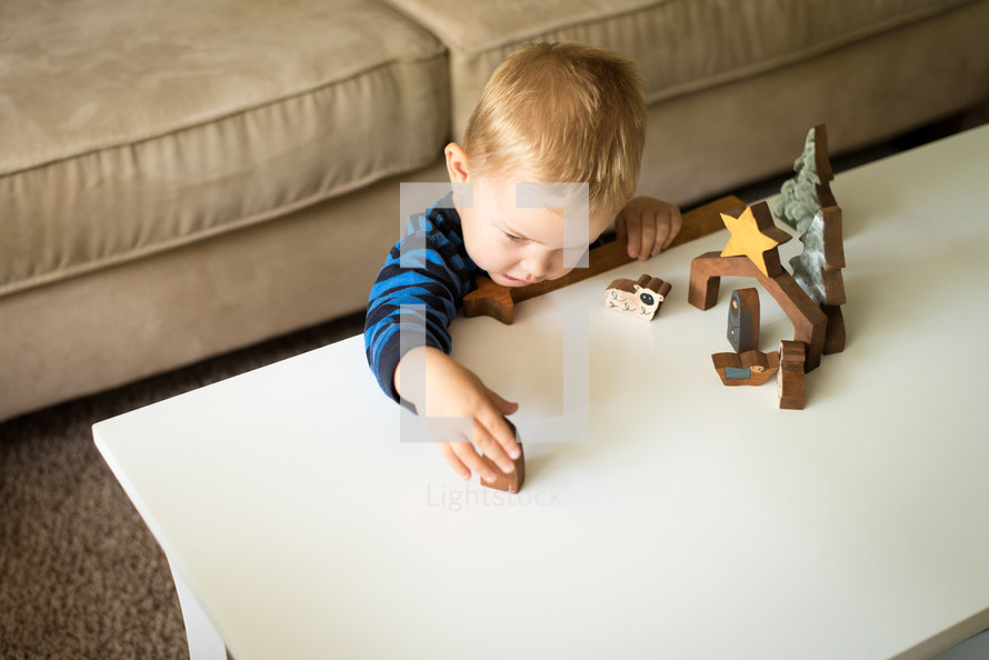 a toddler playing with wooden nativity figurines 