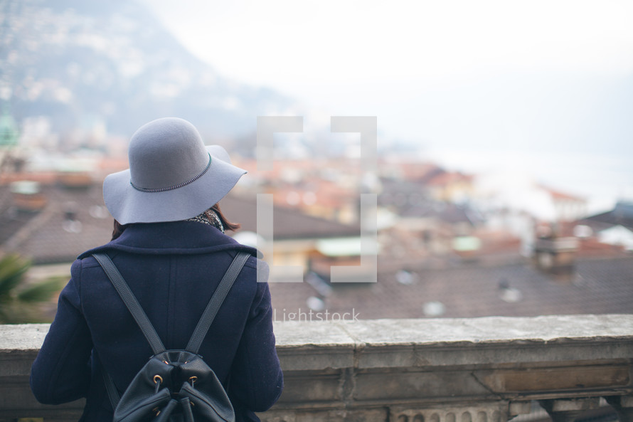 a woman in a peacoat and hat looking out over a railing 