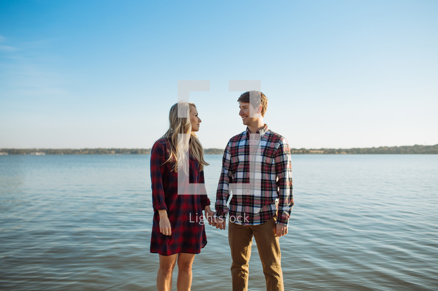 a couple holding hands standing on a lake shore 