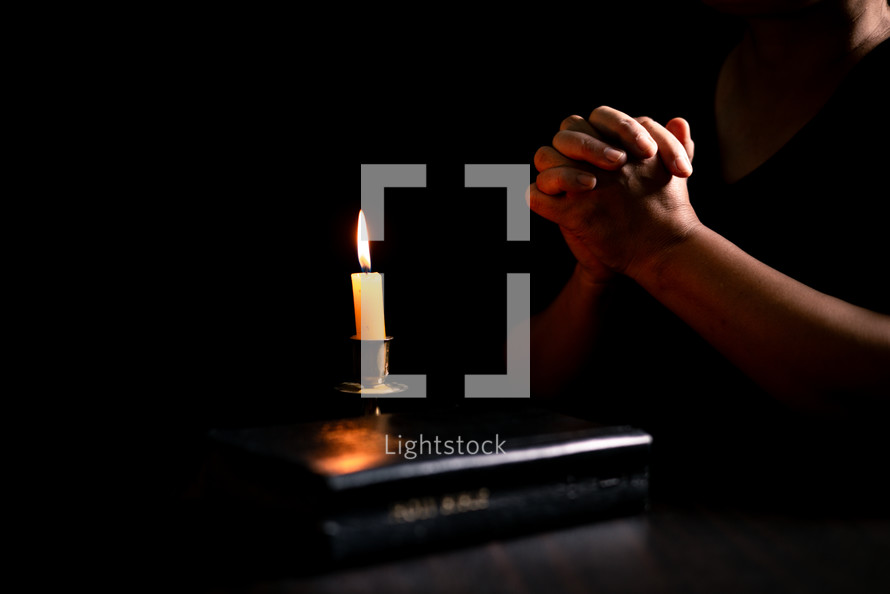 Bible and candlelight with praying hands