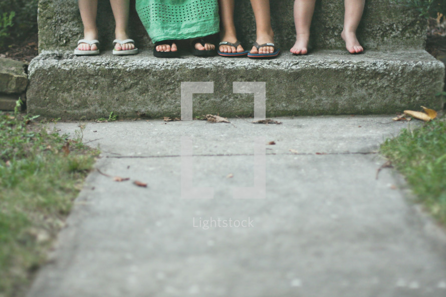 Kids' feet on a cement step.