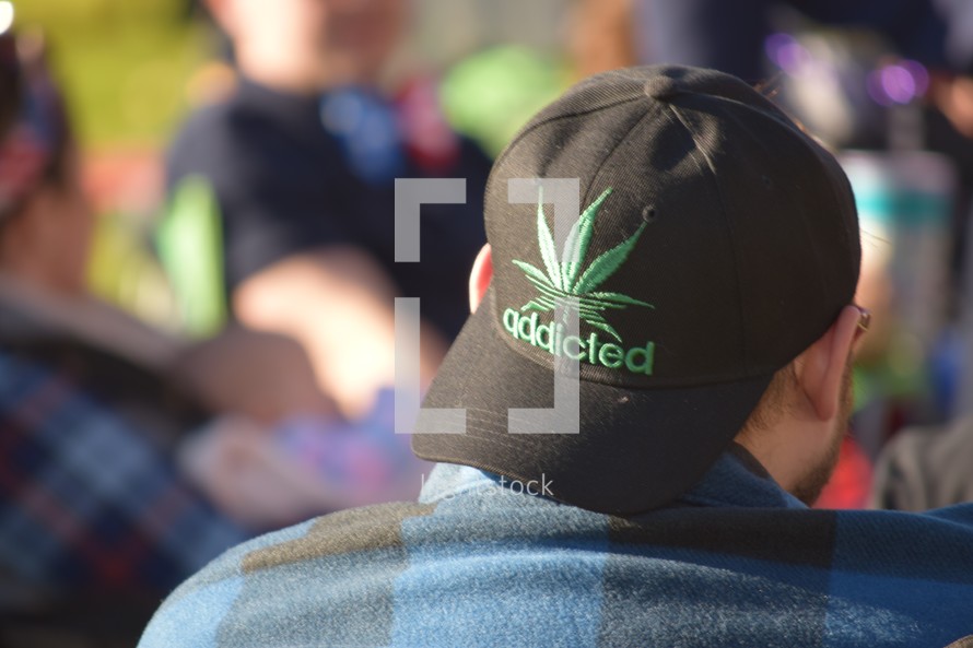 A man wearing a Marijuana leaf hat with the word addicted 
