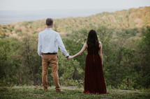 couple holding hands standing on a hill 