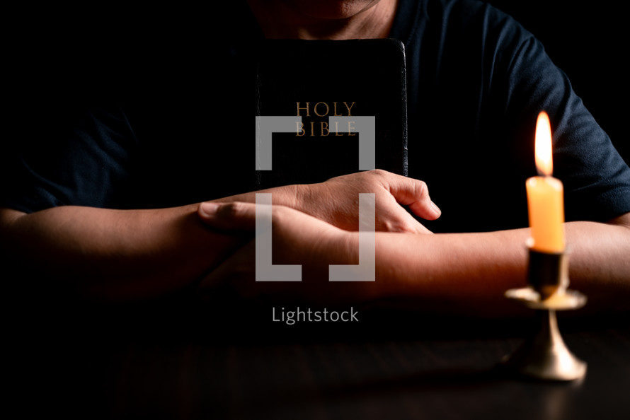 Bible and candlelight with praying hands