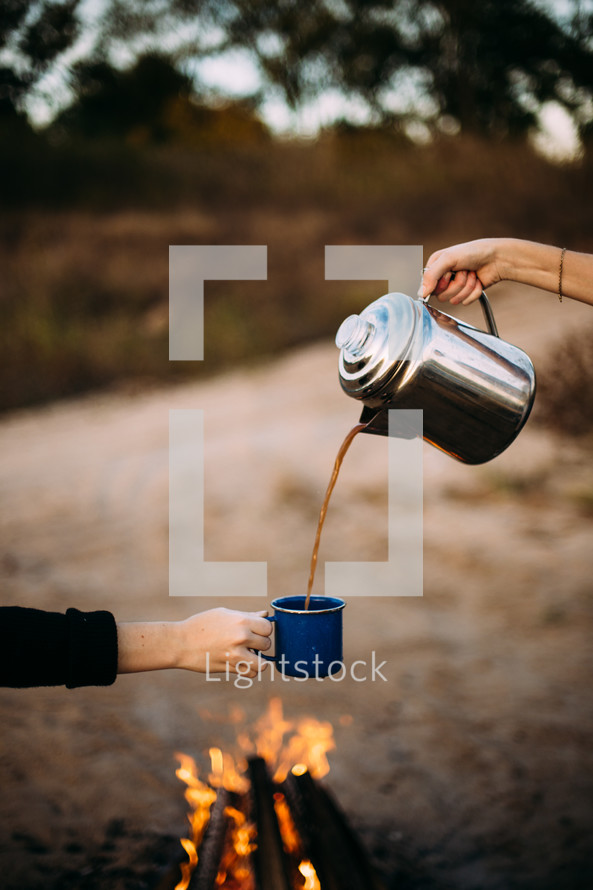 pouring coffee from a coffee pot into a mug over a campfire 