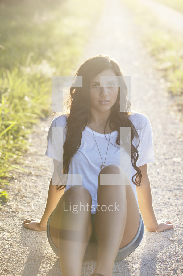 woman sitting on a dirt road under the glow of sunlight 