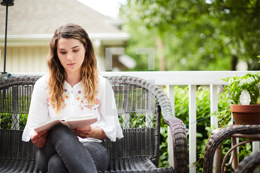 a woman sitting on a porch reading a Bible 