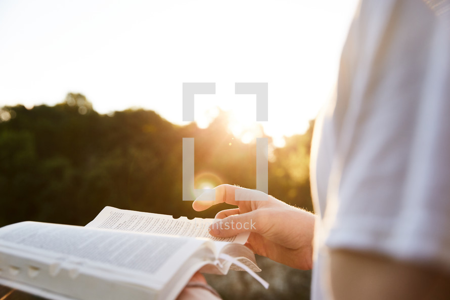 a woman turning the pages of a Bible outdoors in sunlight 