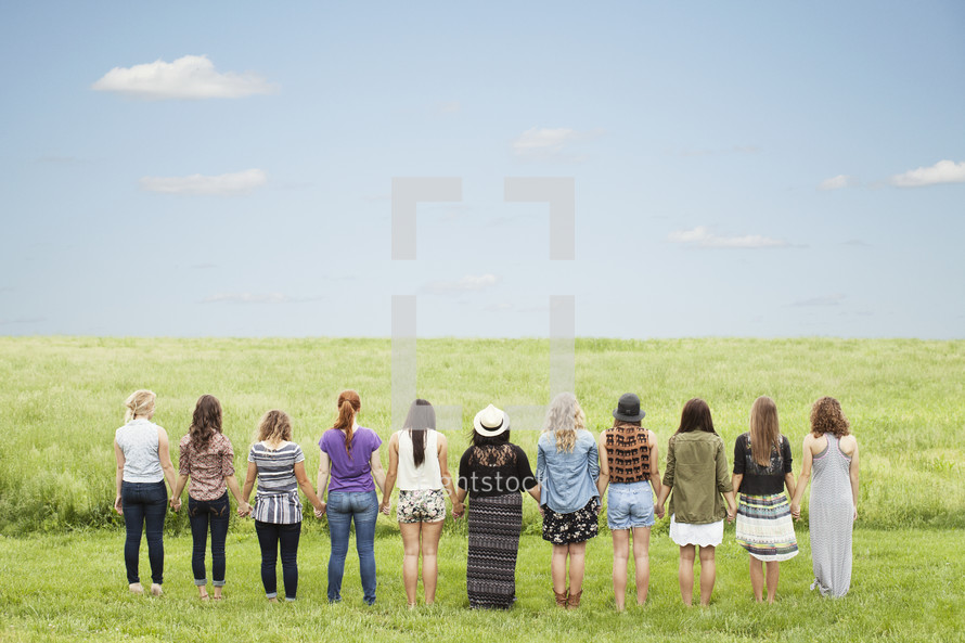 Line of women standing outside in a field holding hands.