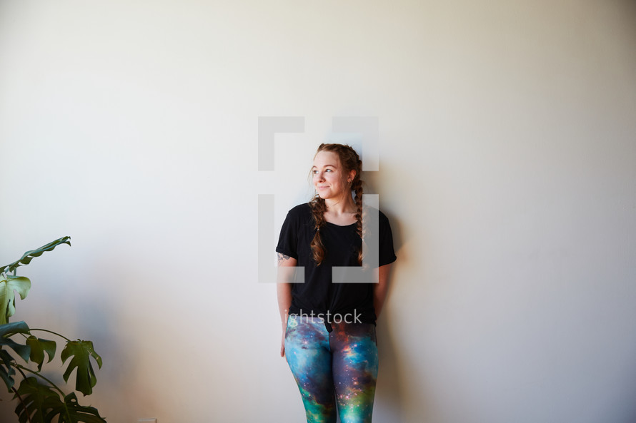 a woman in yoga pants leaning against a white wall 
