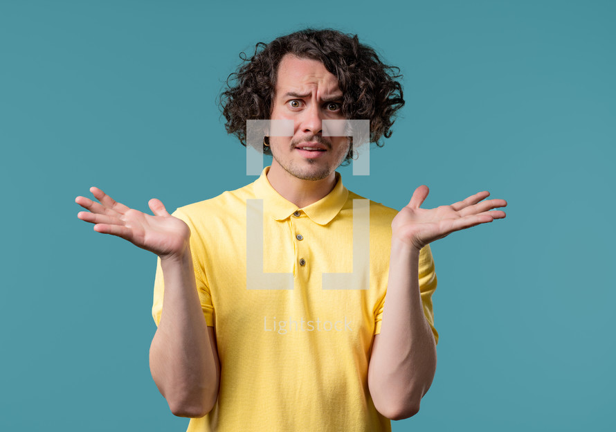 Confused man, shoulders up - can't help, makes gesture of I dont know. Difficult question, guilty reaction, puzzled teenage guy on blue background. High quality