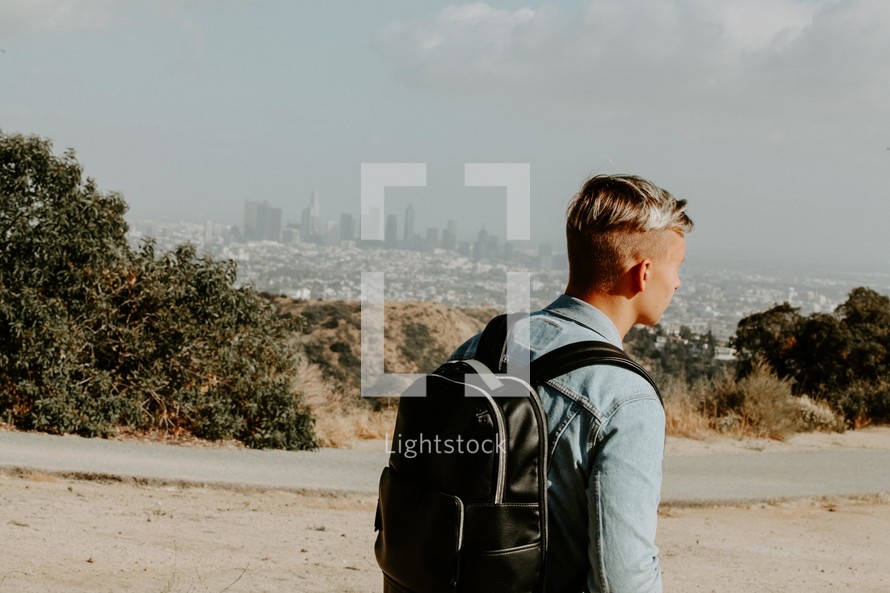 young man with a book bag and distant city view