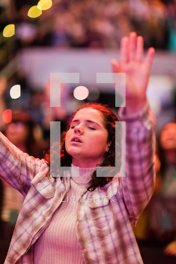 A young woman with arms raised in a worship service.