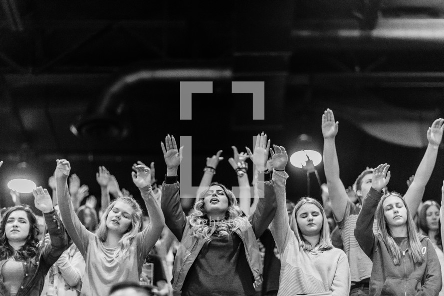 Young people with their hands raised in a worship service.