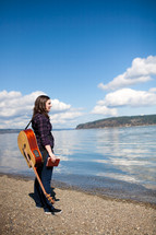 woman standing by a lake with a Bible and guitar 