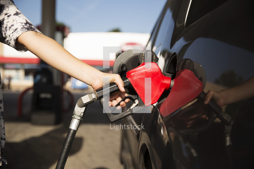 a woman filling up her car with gas at a gas station.