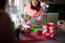 A woman in a santa hat smiling and wrapping Christmas presents