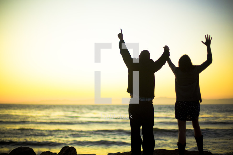 couple with raised arms on a beach - worship to God