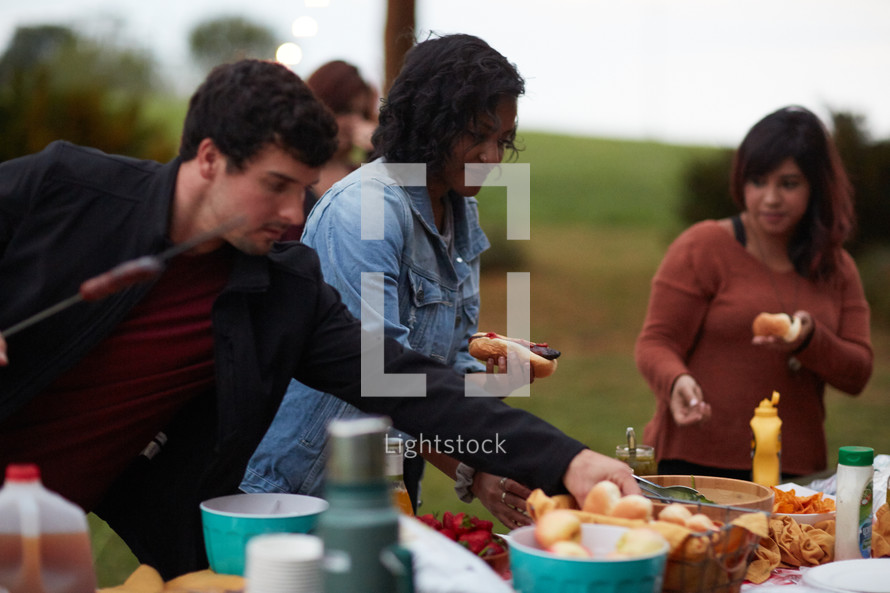 friends gathered around a table getting food at an outdoor party 