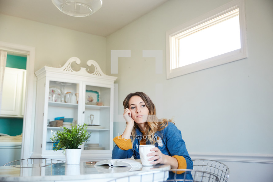a woman sitting at her kitchen table by herself looking away and thinking 