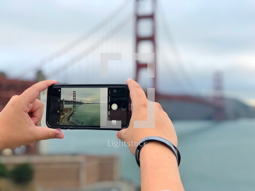 a woman taking a picture of the Golden Gate Bridge with her cellphone 