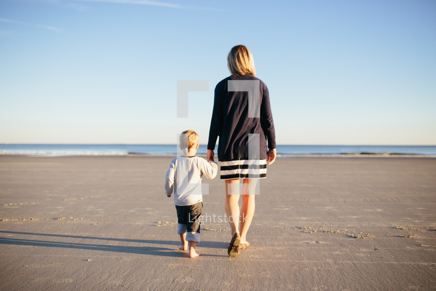 mother and son walking holding hands on a beach 