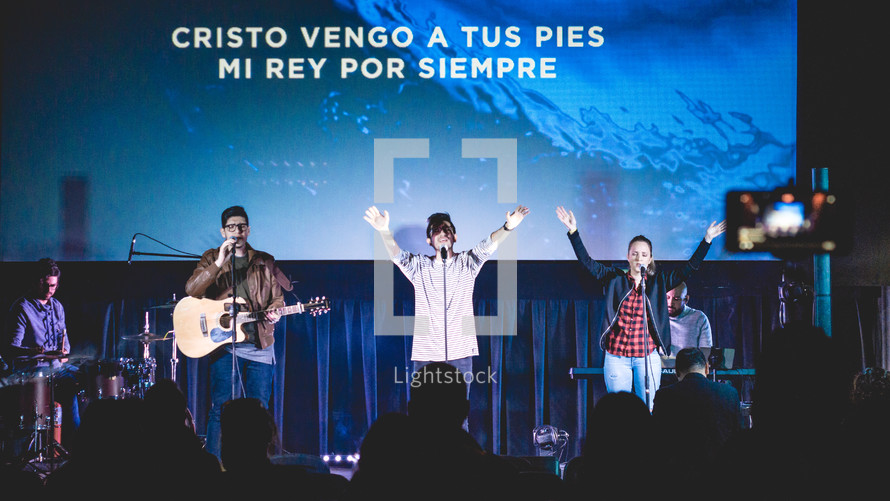 worship leaders performing on stage in front of a projection screen with Spanish lyrics 