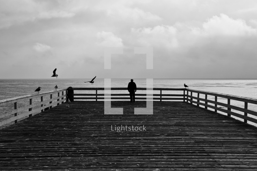man looking at the ocean from a pier 