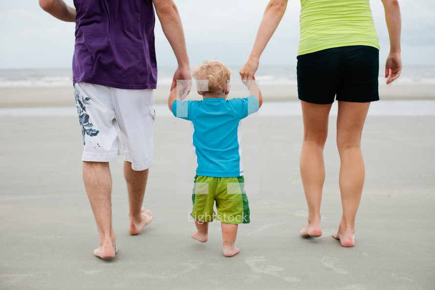 mother, father, and son holding hands walking on a beach 