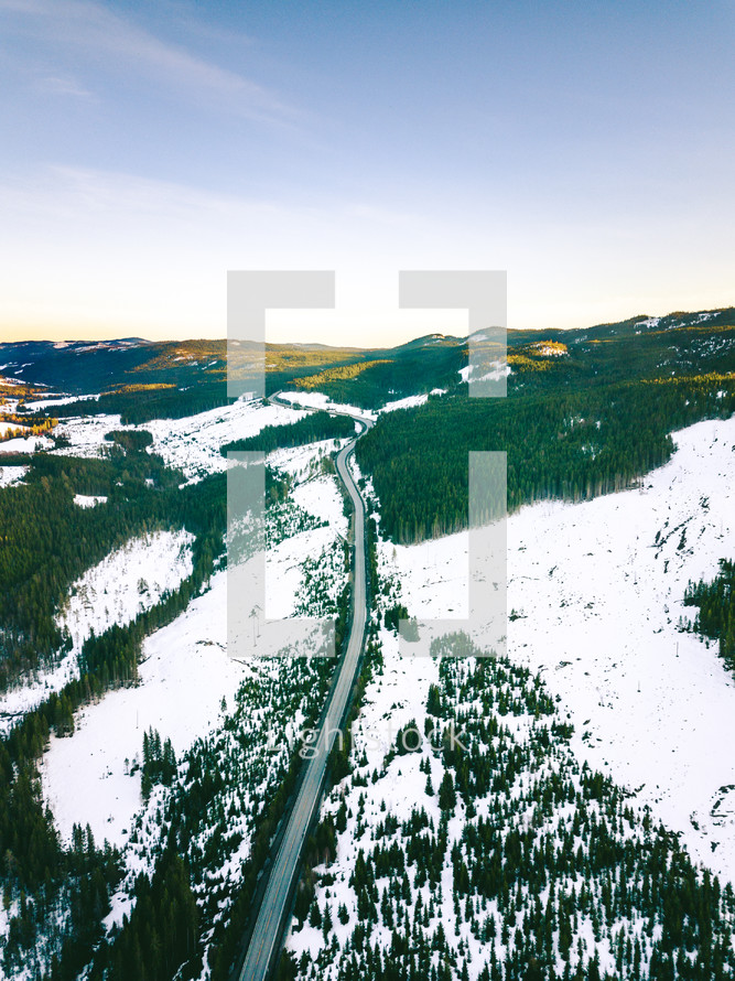 aerial view over a road through an evergreen forest in winter 