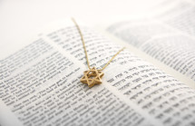 Open Hebrew/English Bible with a gold Star of David pendant on the page.